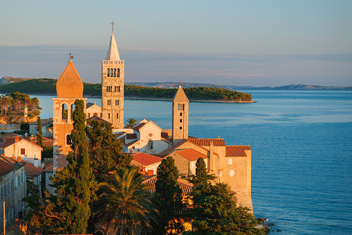 Beautiful view on church towers, littoral trees and house rooftops in Rab old town at sunset, Rab island in Croatia