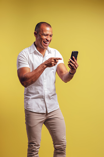 Portrait of a Brazilian wearing a button-up shirt and jeans, smiling and looking at his cell phone, while pointing at it - Belém - Pará - Brazil
