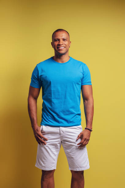 基本的な青いシャツとショートパンツを着て、ポケットに手を入れて微笑んでカメラを見ているブラジル人のポートレート - ベレン - パラ - ブラジル - handsome man flash ストックフォトと画像