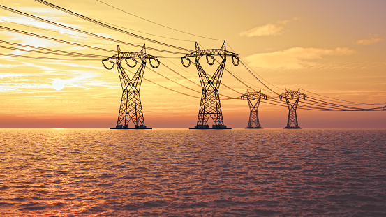 The silhouette of the high voltage power lines on the sea during sunset.