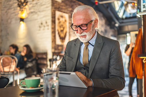 One Senior man caucasian male businessman business owner use digital tablet sit at cafe wear suit copy space