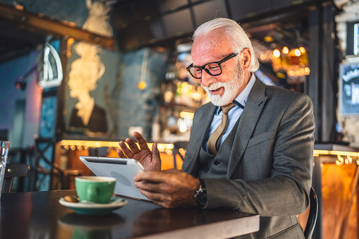 One Senior man caucasian male businessman business owner use digital tablet sit at cafe have video call talk connection and communication wear suit copy space