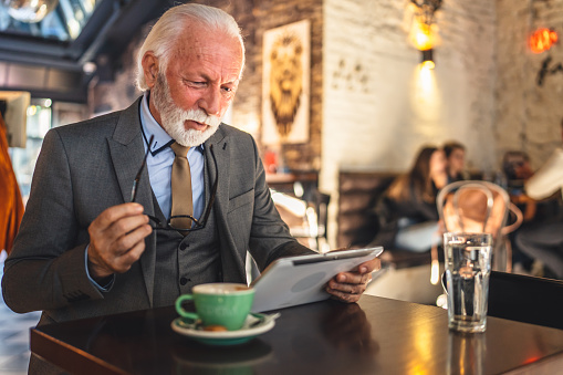 One Senior man caucasian male businessman business owner use digital tablet sit at cafe wear suit copy space worried thinking bad news solve problem