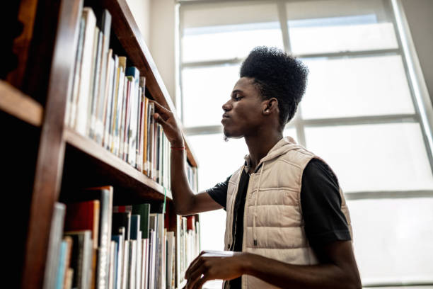 istock Young man searching a book on the shelf in the library 1493271898