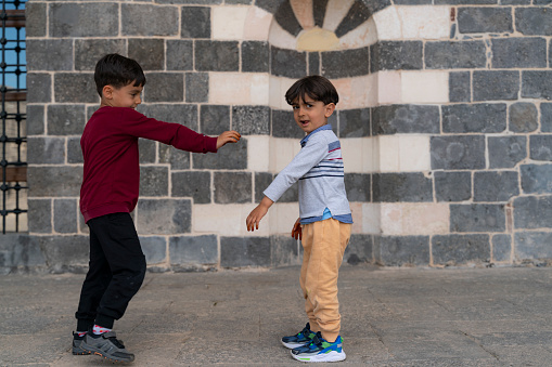 image of brothers playing in front of historic stone house.Historic house made of wooden door and volcanic stone. brothers spending time together in street. Shot with a full-frame camera in daylight.