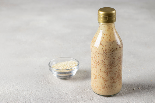 Sesame salad dressing in a bottle and sesame seeds in bowl on a gray background, Copy space