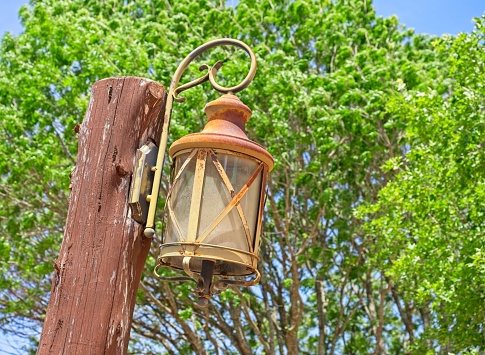 Antique lantern against a green tree background. Rust colored lantern contrasts with green vegetation.