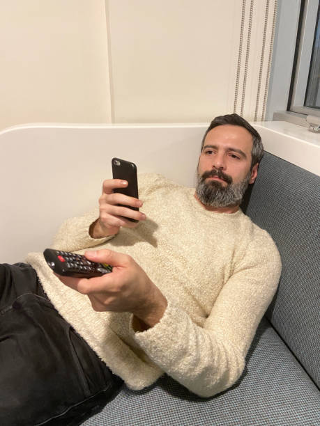 hombre viendo la televisión y sus manos sosteniendo el control remoto y el teléfono inteligente en la sala de estar - 16490 fotografías e imágenes de stock