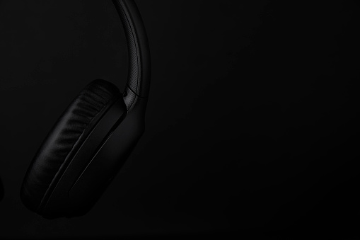 Still life photo of a detail of black headphones on black background with copy space in low key lighting.