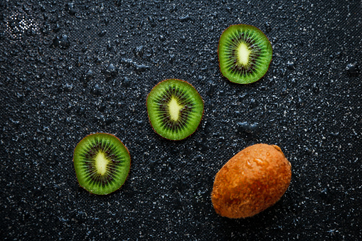 photo of tropical kiwi fresh slices sliced on black background with water drops