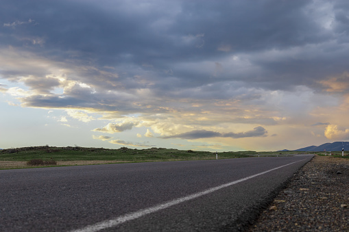 Scenic perspective of an empty highway against a vibrant backdrop of dramatic, colorful clouds during the golden hour