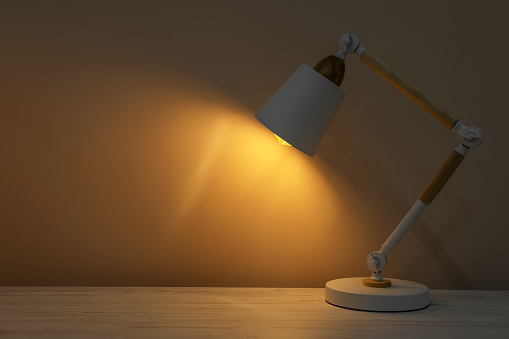 Stylish modern desk lamp on wooden table at night, space for text