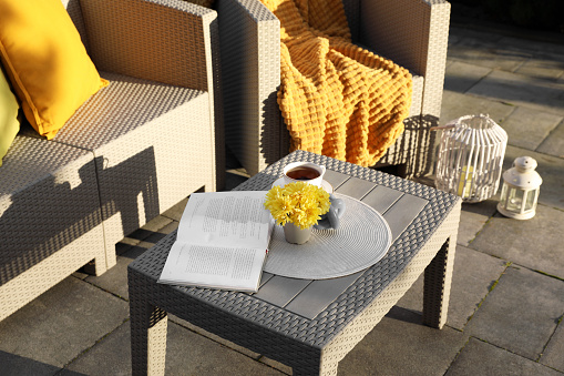 Beautiful rattan garden furniture, cup of tea and different decor elements outdoors