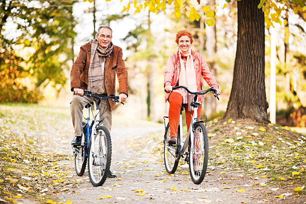 adulto in età matura coppia biciclette equitazione nel parco. - mature adult bicycle senior adult heterosexual couple foto e immagini stock