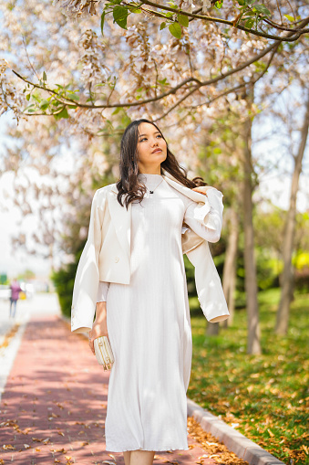 Happy young asian woman in white dress under flowering tree in spring. relax mode