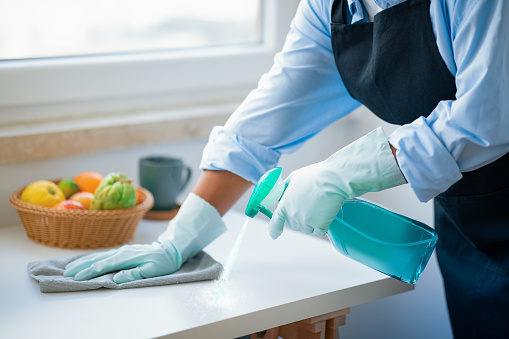 Unrecognizable tidy african american woman in workwear maid cleaning kitchen, female hands using detergent spray and duster cloth, cropped. House-keeping service, professional cleaning