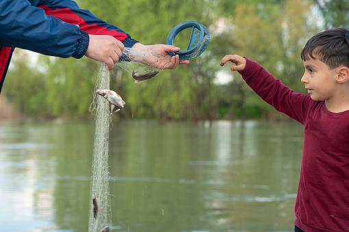 Father and son stretching a fishing rod with fish on the hook while little boy looking excited and keeping mouth open