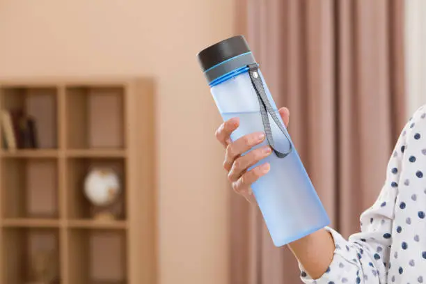 Woman with bottle of water in room, closeup. Space for text