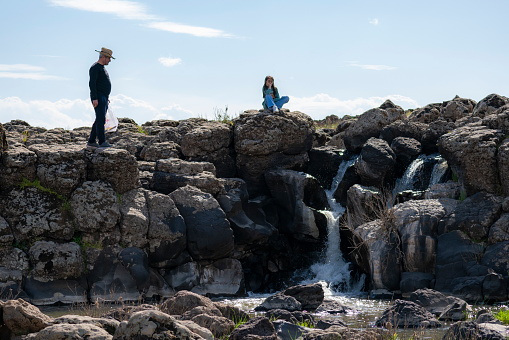 father and daughter watching the view of the small waterfall flowing from the cliffs. In the spring season, water pours from the rocks. father and daughter in a cowboy hat intertwined with nature. Shot with a full-frame camera in daylight.