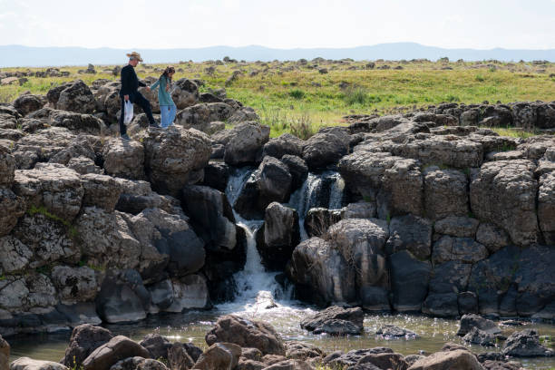 father and daughter watching the view of the small waterfall flowing from the cliffs. In the spring season, water pours from the rocks. father and daughter in a cowboy hat intertwined with nature. Shot with a full-frame camera in daylight.