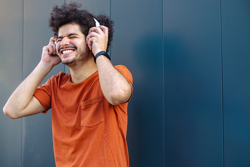 Shot of a young smiling man using wireless headphones and enjoying music