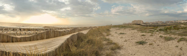 ein hölzerner fußgängerweg, der über einer sanddüne gebaut wurde, die für den zugang zum strand von furadouro verwendet wird, leuchtet bei sonnenuntergang. ovar, aveiro, portugal, europa - beach boardwalk grass marram grass stock-fotos und bilder
