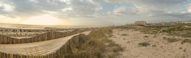 drewniane chodniki dla pieszych, zbudowane nad wydmą, która służy do zapewnienia dostępu do plaży w plaży furadouro, świeci o zachodzie słońca. ovar, aveiro, portugalia, europa - beach boardwalk grass marram grass zdjęcia i obrazy z banku zdjęć