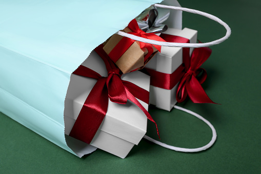 Turquoise paper shopping bag full of gift boxes on green background, closeup