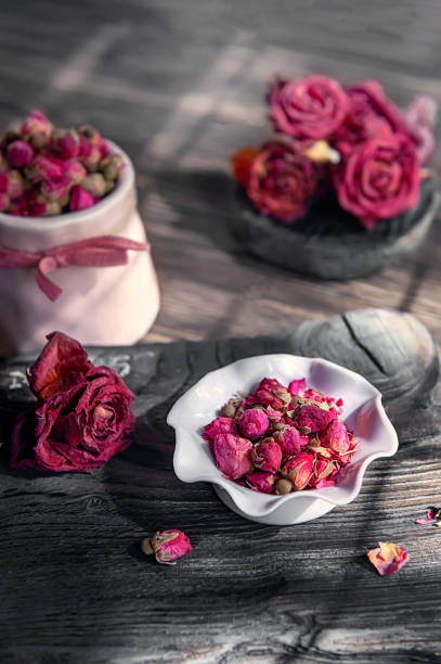 on a wooden table there is a pink vase with rosebud tea. Tea time, cozy atmosphere. Kitchen still life with pink floral tea on the background of contrasting morning light.