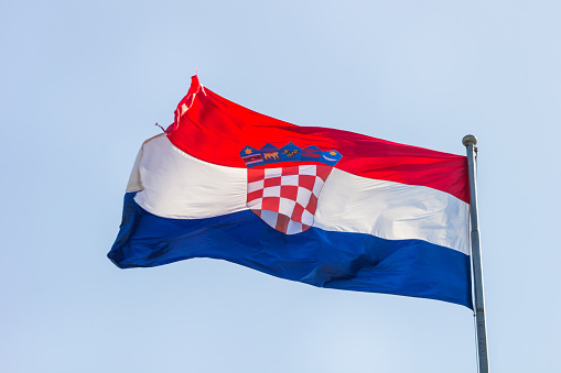 Flag of the Republic of Croatia waving in the wind on flagpole against the sky on sunny day, banner, close-up