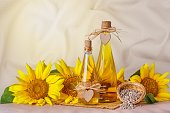 Rural still-life - sunflower oil in glass bottles with flowers of sunflower (Helianthus annuus) against the background of woolen fabric