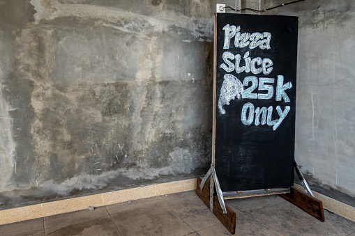 Canggu, Bali, Indonesia, A sign asdverising ofr a slive of pizza for 25 k Indonesian rupiah.