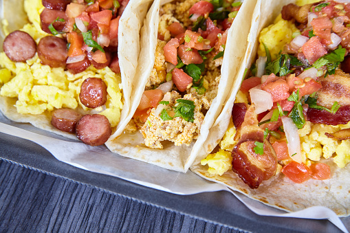 Image of 3 breakfast tacos Mexican Hispanic with egg toppings cilantro, onion, and tomato