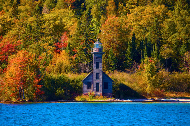 istock Lighthouse with boarded up windows on a distant shore colorful fall trees and sapphire lake water 1493310033