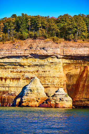 Image of National Park Pictured Rocks collapsed cliff wall jutting out of indigo lake water with forest above