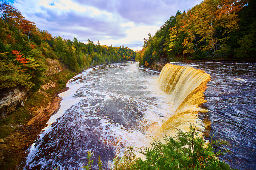 Image of Tahquamenon Falls waterfall with large basin, white flowing river rapids, and green fall forest