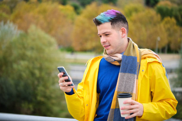 Man wearing a yellow raincoat with a coffee using a phone in autumn. stock photo