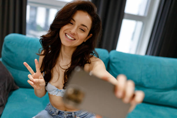 istock Cheerful dark-haired young pretty lady taking a selfie with her mobile phone while sitting on the comfortable sofa in the living room. Modern lifestyle concept 1493312276