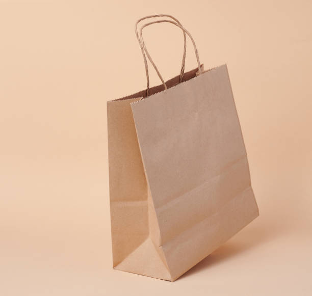 istock Disposable brown kraft paper bag with handles on beige background, eco packaging, zero waste 1493313276