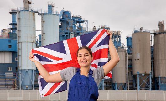 Smiling young woman in uniform posing with UK flag near factory