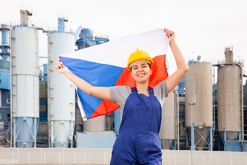 Happy woman waving flag of Czech Republic against the background of a modern factory