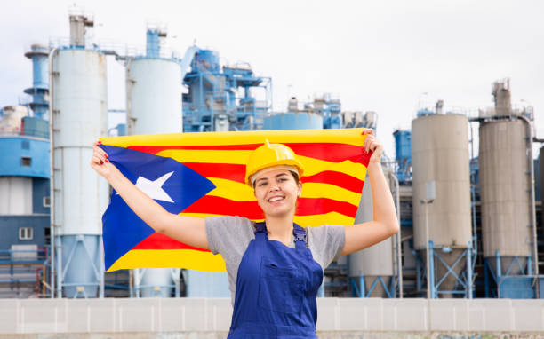 glückliches mädchen in arbeitskleidung und schutzhelm mit flagge von katalonien, das vor einer industrielandschaft steht - catalonia success confidence flag stock-fotos und bilder