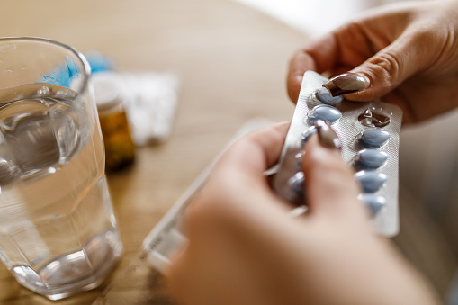 Close up shot of unrecognizable young woman sitting at coffee table, sorting out and organizing her medication, for the week, in a pill organizer box.