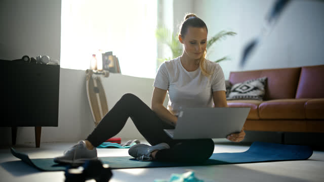 SLO MO Fit young woman with laptop preparing for online home workout on yoga mat on living room floor. Healthy lifestyle,exercise,fitness,active lifestyle,domestic life. Shot in 8K Resolution.