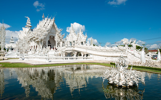 In Chiang Rai, Thailand the White Temple reflection shows clearly in the surrounding pool of water on a bright sunny day.