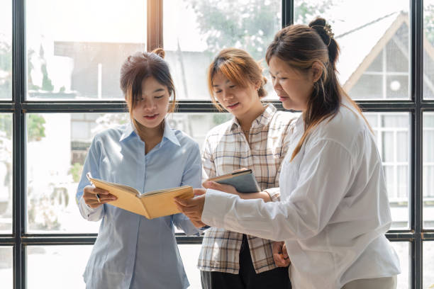 istock Beautiful young woman reading book with classmates studying in background. University students studying together in class 1493352511