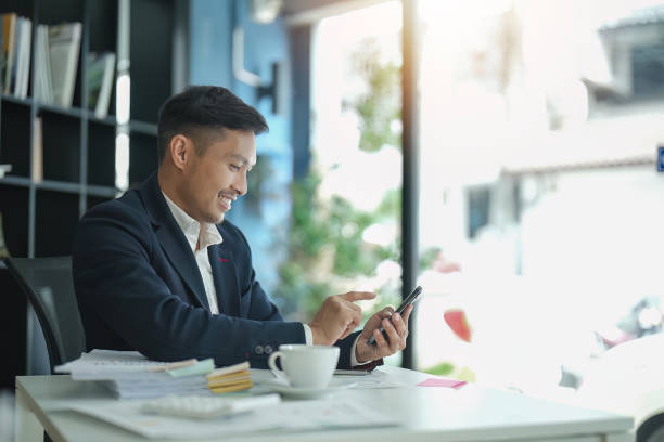 istock Happy young Asian business man with a smile using smartphone at the office 1493352694