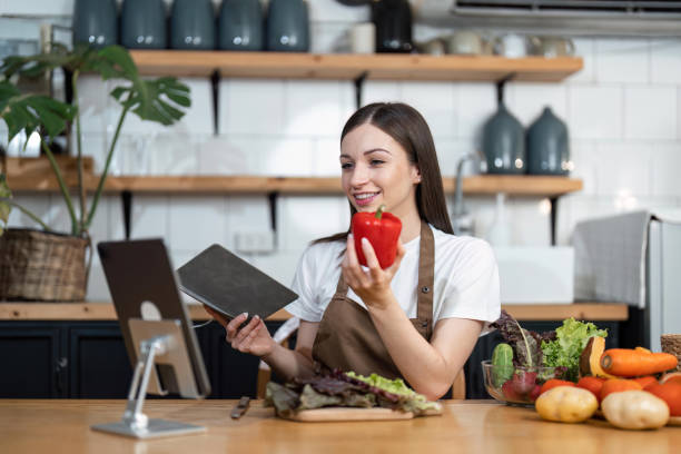 istock Image of young pretty lady in kitchen and cooking the salad. Looking at tablet computer 1493364616