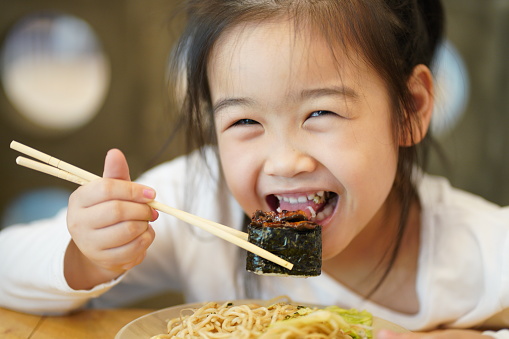 Young asian children enjoy eating Yakisoba and Sushi by using chopsticks