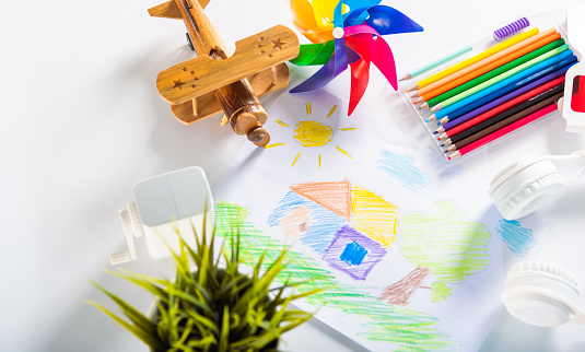 Child colorful drawing landscape my home dream on white paper, kid preschooler draw country house picture with pencil on table, arts homework concept